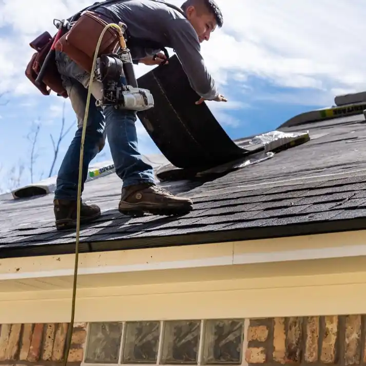 A roofer laying a shingle course along the eave