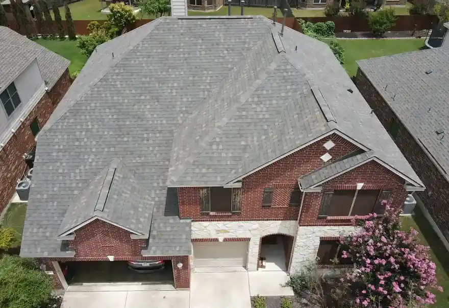 Drone view of a two-storey brick home with a new grey shingle roof and a pink crepe myrtle in the yard
