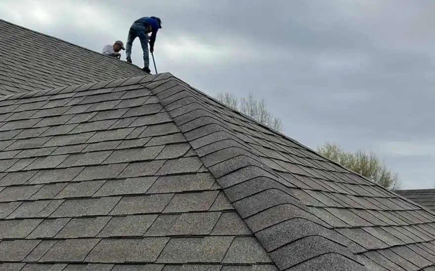 A Steele inspector crouched on a steep grey shingle roof, checking the courses by hand