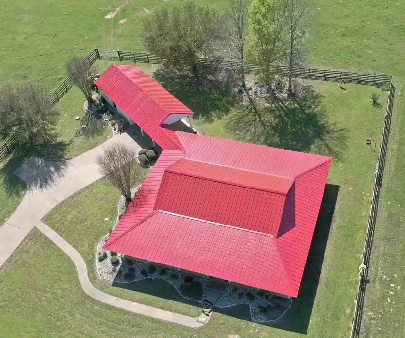 Drone view of a red metal roof on a ranch home beside a fenced pasture