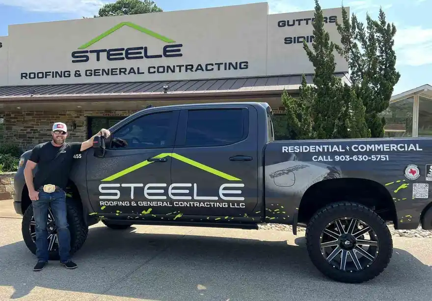 A man leaning on a Steele Roofing truck outside the office