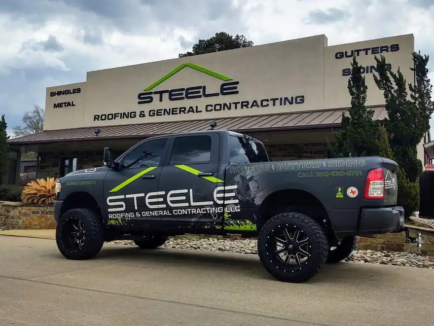 A wrapped black Steele Roofing pickup parked at the office sign on Hwy 69 South